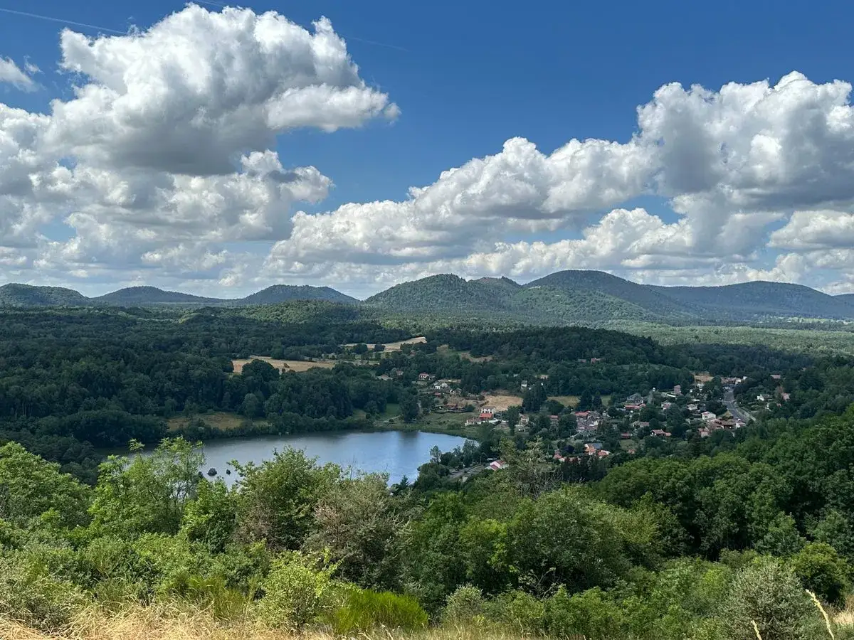 Vue panoramique sur le lac de Cassi&egrave;re, entour&eacute; de collines verdoyantes et d'un village pittoresque sous un ciel bleu parsem&eacute; de nuages blancs.