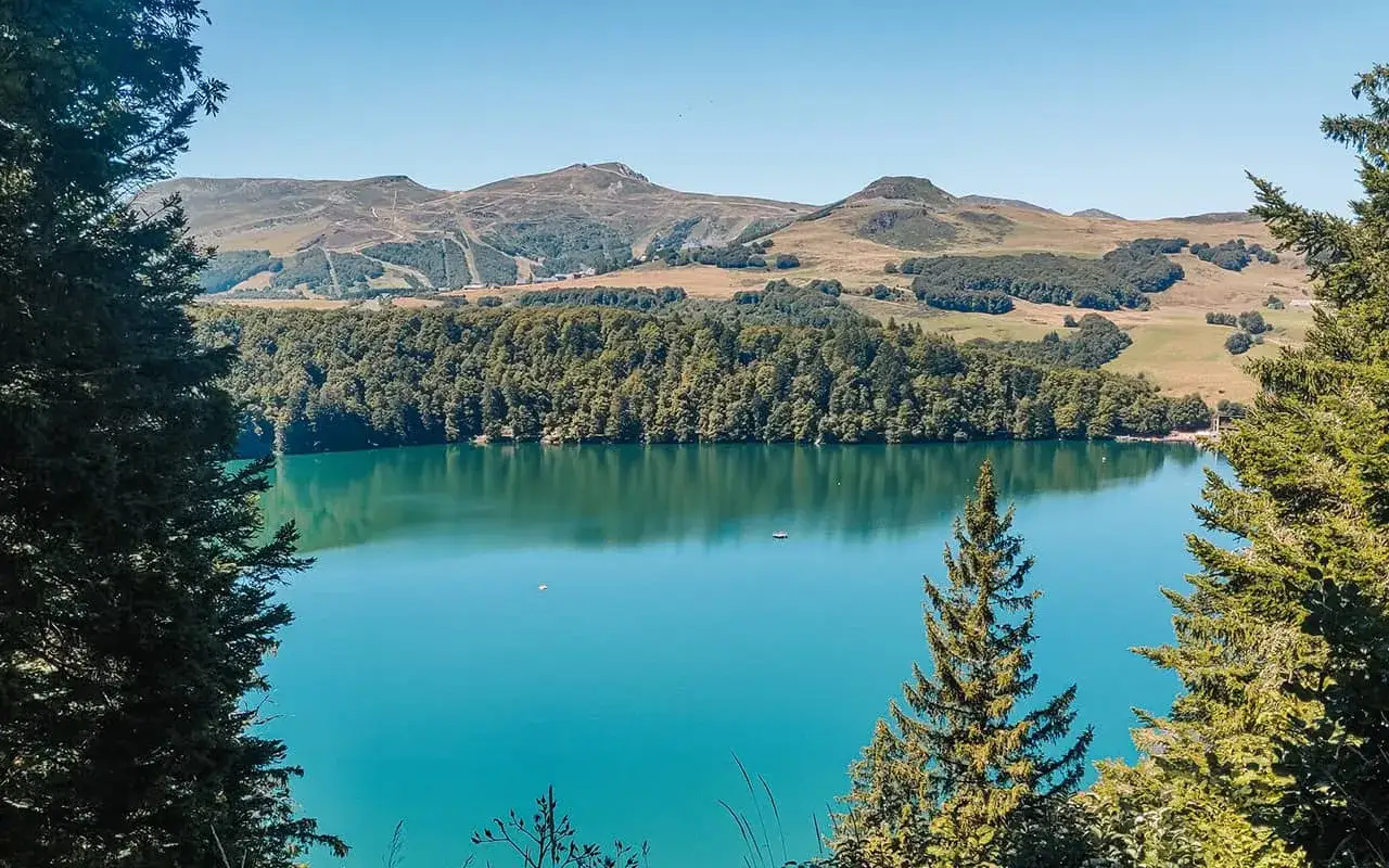 Vue magnifique d'une randonnée au lac Pavin, avec ses eaux turquoise, la forêt dense et les montagnes en arrière-plan.