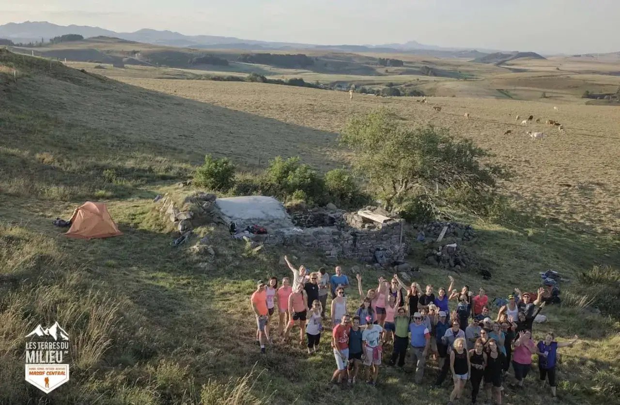 Un groupe joyeux pose près d'un abri en ruine, avec une tente orange et un paysage vallonné en arrière-plan. Le signal du Luguet est peut-être à proximité.