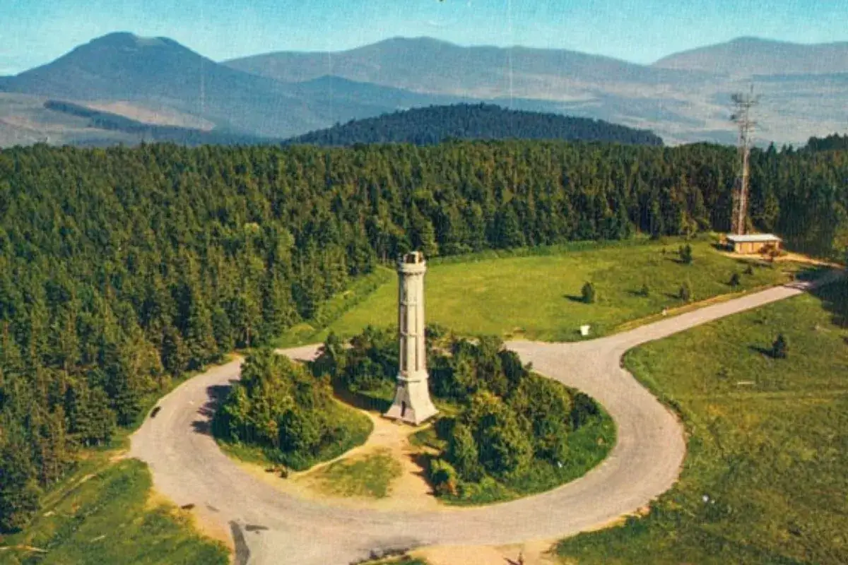 Tour panoramique sur le champ du feu, avec une tour de guet, une forêt dense et des montagnes en arrière-plan.