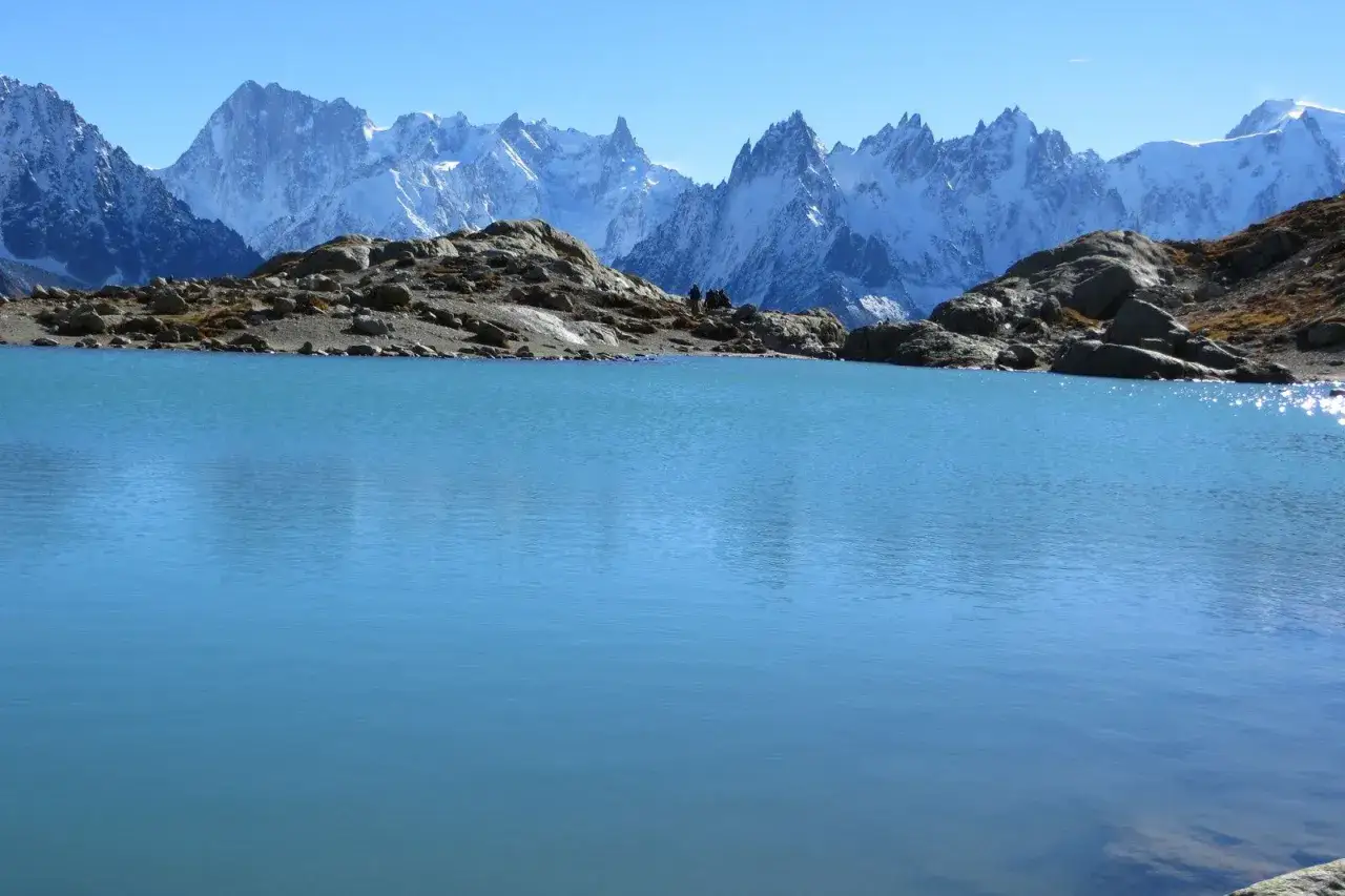 Lac d'altitude aux eaux turquoises, bord&eacute; de rochers, avec en arri&egrave;re-plan les sommets enneig&eacute;s des Aiguilles Rouges. Un moment de qui&eacute;tude lors d'un trek.