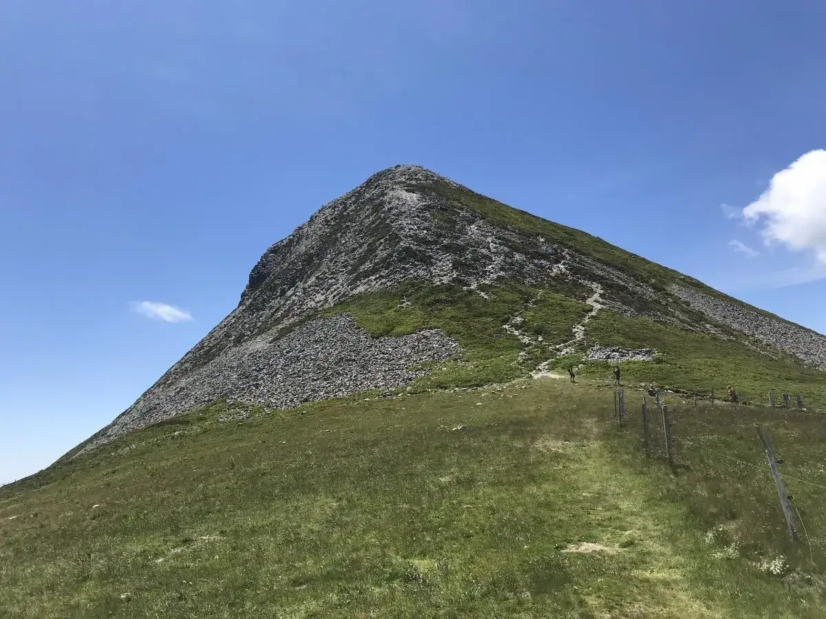 Sentier menant au sommet du Puy Griou, un volcan d'Auvergne. Des randonneurs gravissent la pente verdoyante et rocailleuse sous un ciel bleu.