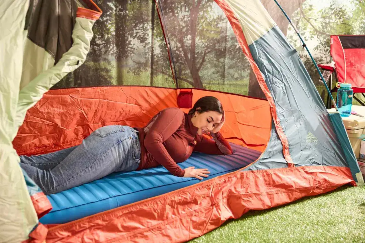 Une femme se repose sur un matelas gonflable dans une tente. Elle se demande combien de temps laisser gonfler un matelas pour un confort optimal en camping.