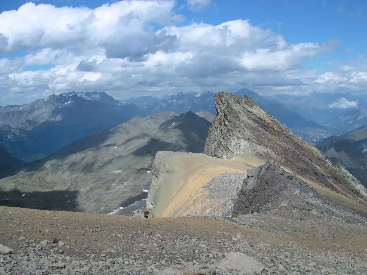 Vue spectaculaire depuis le Mont Thabor, avec des crêtes rocheuses acérées et des montagnes bleutées à l'horizon sous un ciel nuageux.