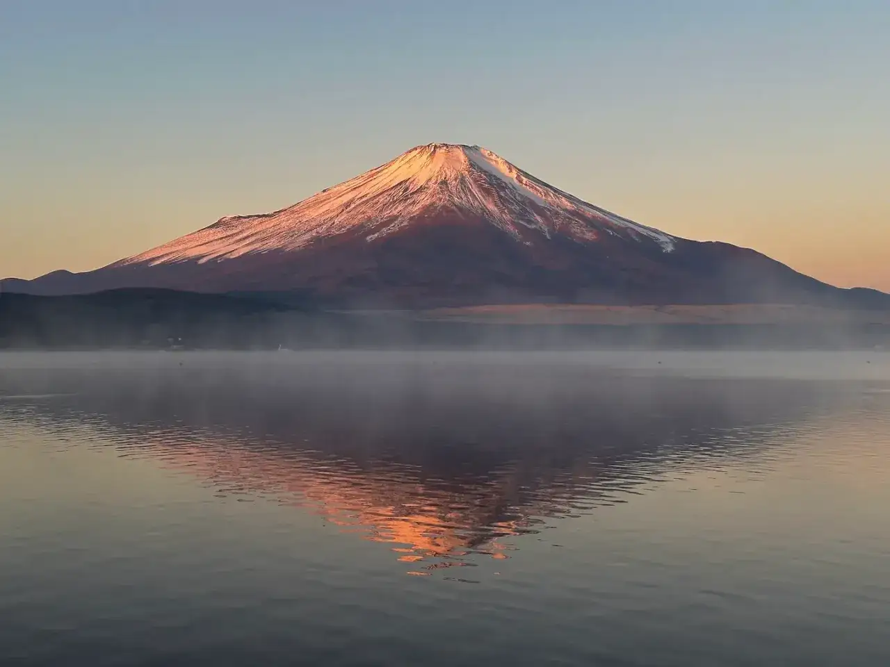 Le Mont Fuji se reflète dans le lac Kawaguchi, baigné par la lumière dorée du lever du soleil.