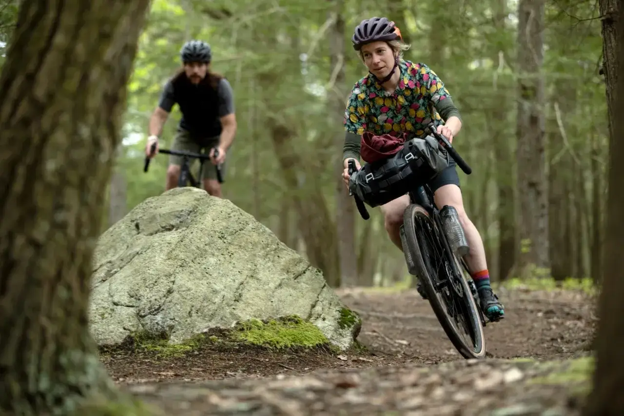 Cyclistes en for&ecirc;t, sacoche sur le guidon, illustrant le bikepacking : voyager &agrave; v&eacute;lo avec son &eacute;quipement.