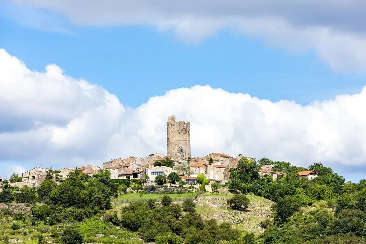 Village médiéval perché avec sa tour de guet, un paysage à voir en Auvergne sous un ciel bleu et nuageux.