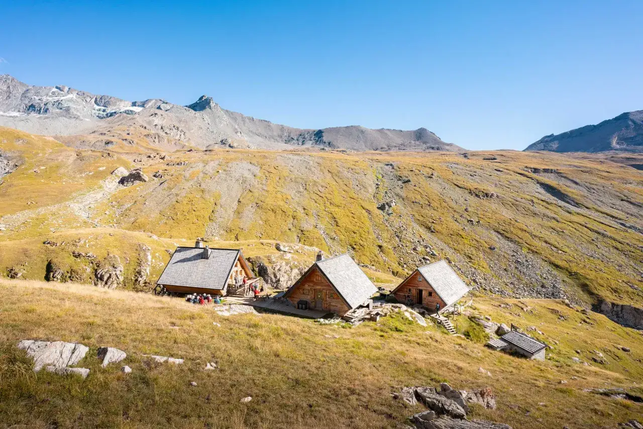 Trois refuges en bois dans un paysage de montagne dor&eacute;, parfaits pour une travers&eacute;e de la Vanoise.
