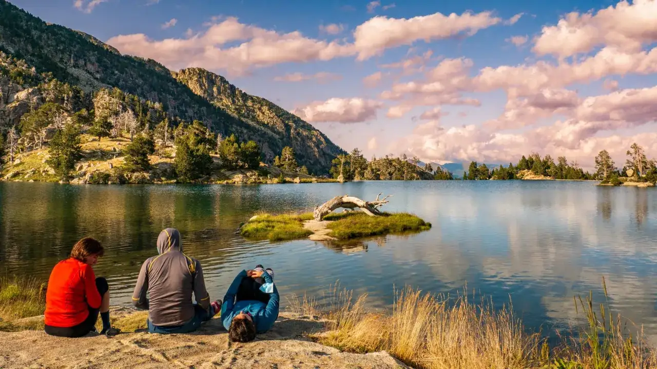 Trois randonneurs se reposent au bord d'un lac de montagne, profitant d'une pause sur la haute route pyr&eacute;n&eacute;enne. Le paysage est spectaculaire.