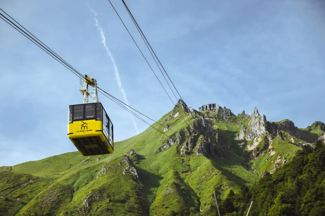 Le funiculaire du Puy de Sancy monte sur une montagne verdoyante sous un ciel bleu.