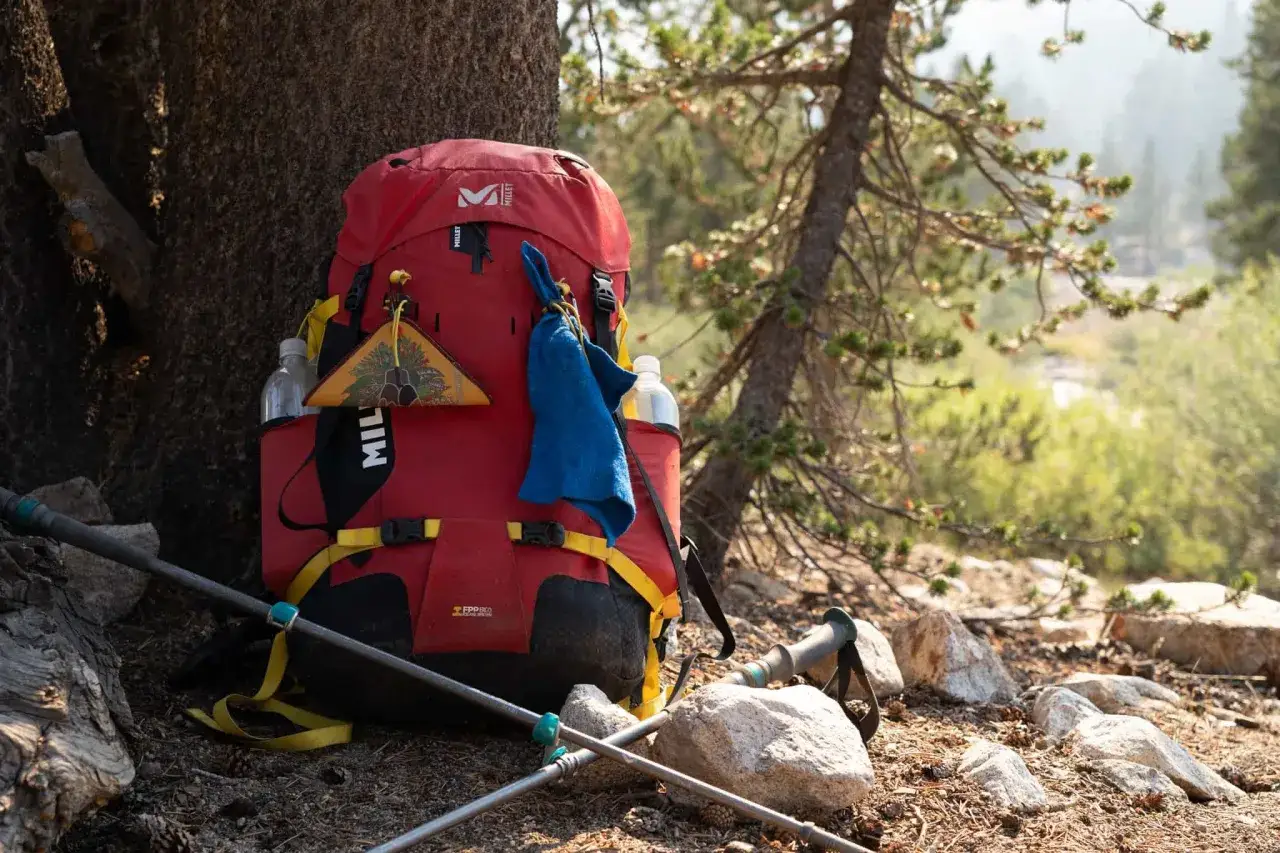 Sac &agrave; dos rouge Millet pr&ecirc;t pour une aventure de 5 jours. Le poids du sac randonn&eacute;e 5 jours est optimis&eacute; pour le confort. B&acirc;tons de marche et gourdes &agrave; port&eacute;e de main.