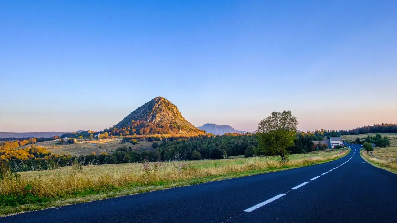 Route sinueuse menant au Mont Gerbier, baign&eacute; par la lumi&egrave;re dor&eacute;e du soleil couchant. Paysage de campagne verdoyante et de for&ecirc;ts automnales.