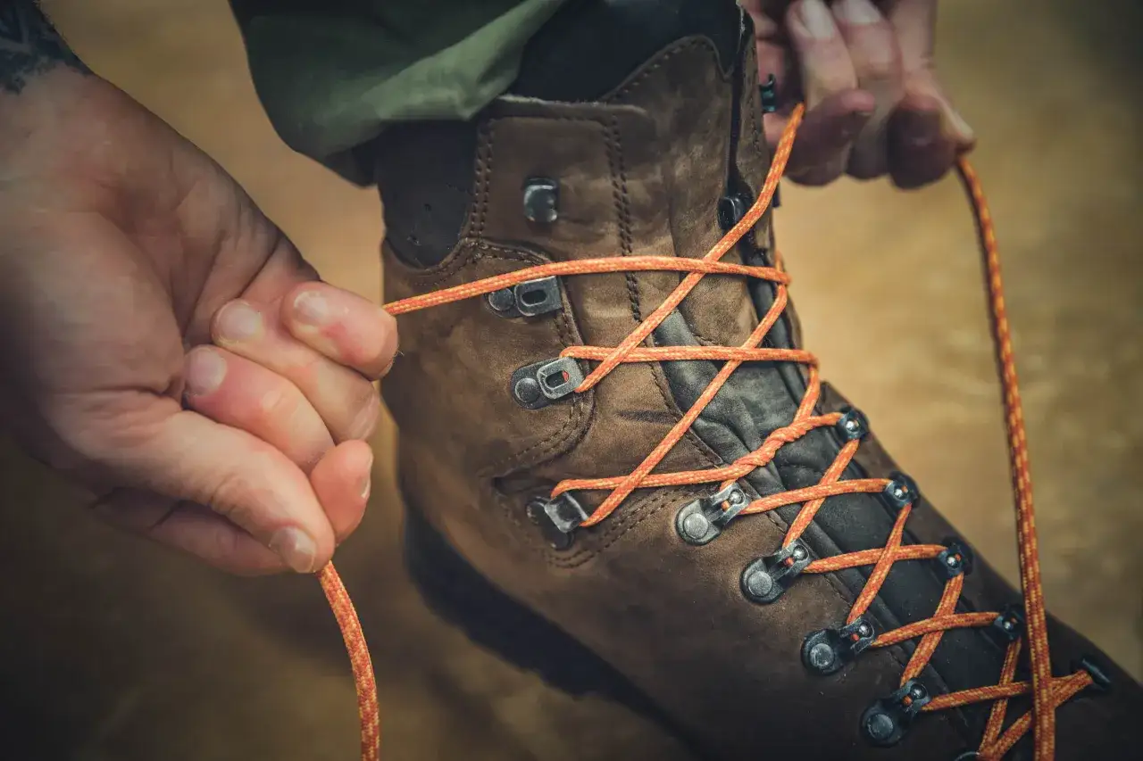 Mains serrant un lacet orange vif sur une botte de randonn&eacute;e marron. Un tuto noeud lacet pour l'aventure.