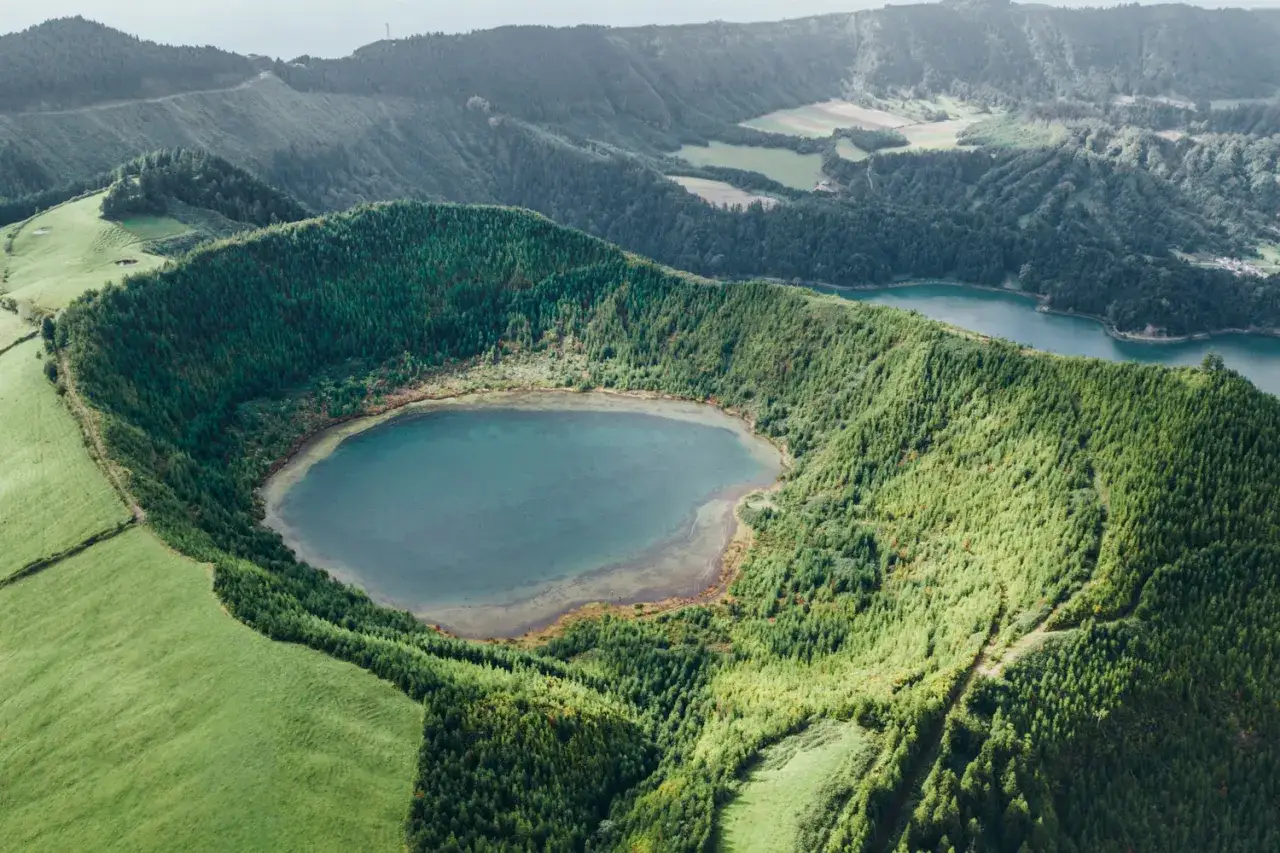 Vue aérienne d'un lac de cratère verdoyant sur l'île de São Miguel, entouré de forêts denses et de prairies.