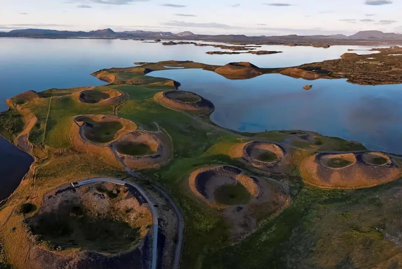 Paysage spectaculaire du lac Myvatn en Islande, avec ses cratères volcaniques verdoyants et ses eaux calmes reflétant le ciel.
