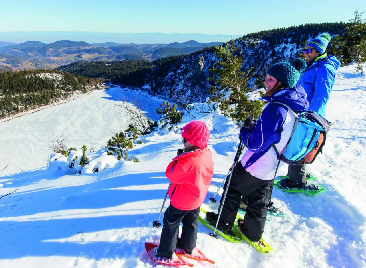 Famille en raquettes admirant un paysage hivernal des skivosges. Le lac gel&eacute; et les montagnes enneig&eacute;es offrent un spectacle magnifique.