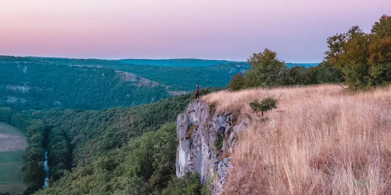 Un homme se tient au bord d'une falaise, contemplant la vall&eacute;e verdoyante. La voie du ciel s'ouvre devant lui, baign&eacute;e par la douce lumi&egrave;re du cr&eacute;puscule.