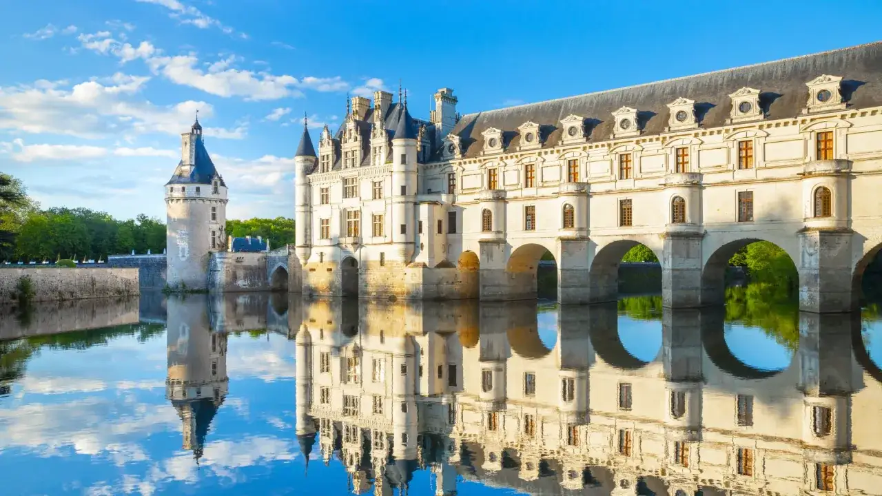 Le Château de Chenonceau, un joyau à visiter dans le Centre de la France, se reflète dans le Cher sous un ciel bleu.