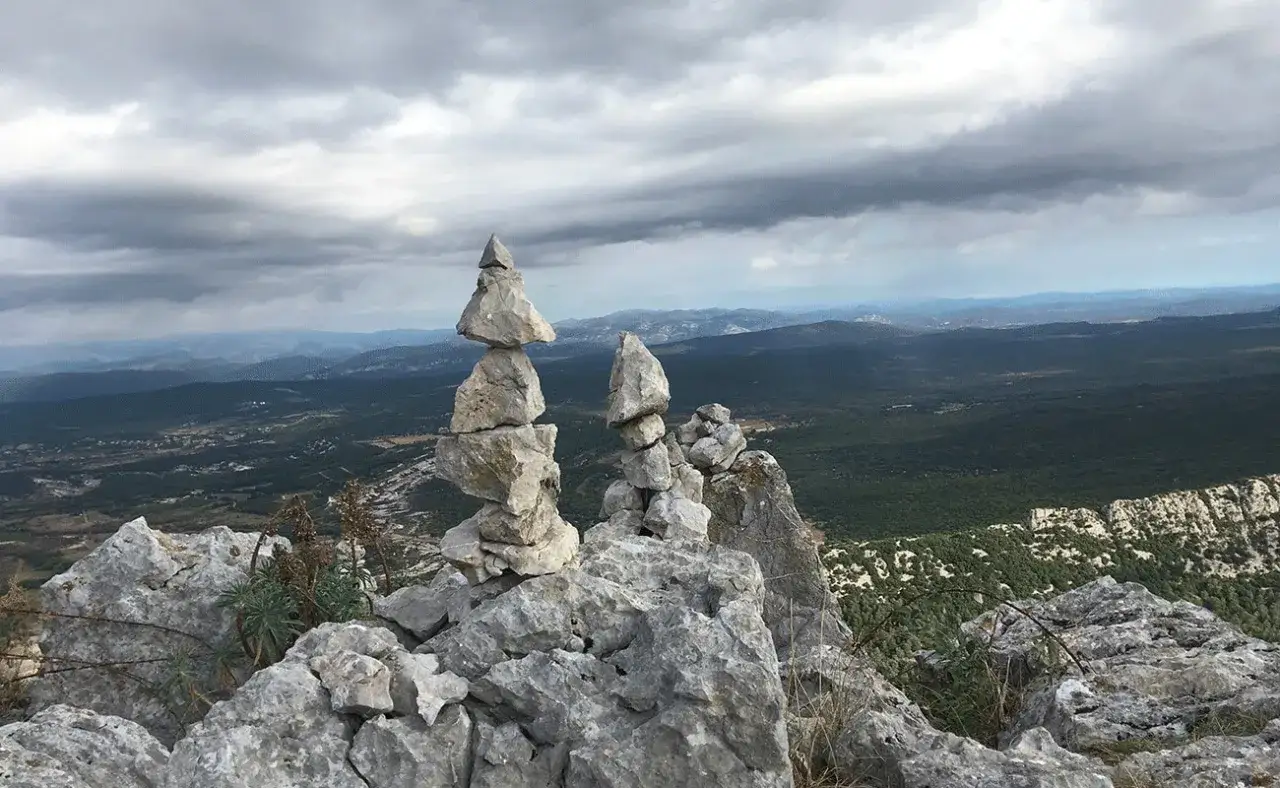 Cairns de pierres sur le pic Saint-Loup, offrant une vue panoramique sur la garrigue et les montagnes sous un ciel nuageux.