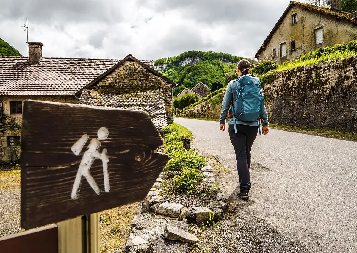 Panneau de randonnée pour débutant indiquant un chemin. Une personne marche sur la route, sac à dos bleu sur les épaules.