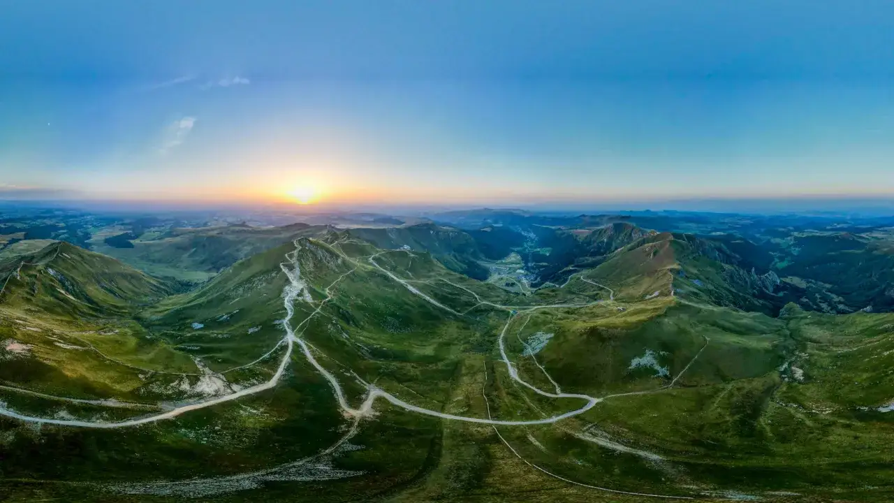 Vue panoramique d'une rando au Puy de Sancy au lever du soleil. Des sentiers serpentent sur les flancs verdoyants des volcans d'Auvergne.