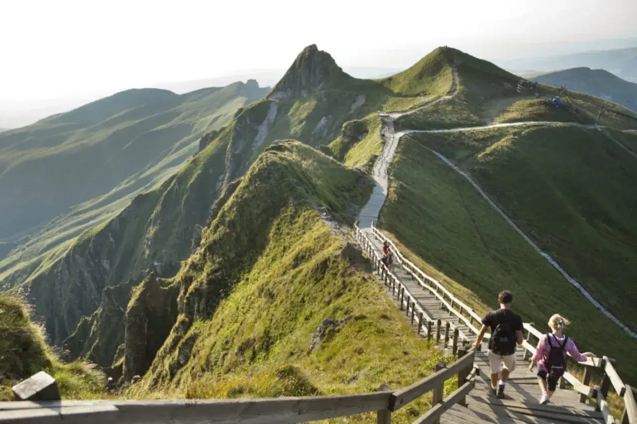 Couple randonnant sur les sentiers de Besse Mont-Dore, paysage de montagnes verdoyantes et de crêtes spectaculaires.