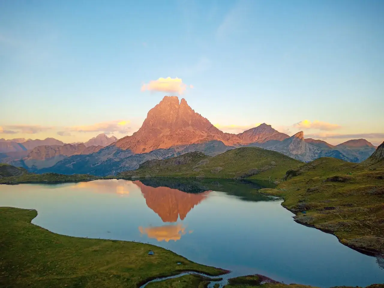 Le pic d'Ayous se refl&egrave;te dans un lac paisible, baign&eacute; par la lumi&egrave;re dor&eacute;e du lever du soleil. Des montagnes majestueuses entourent ce paysage pyr&eacute;n&eacute;en.