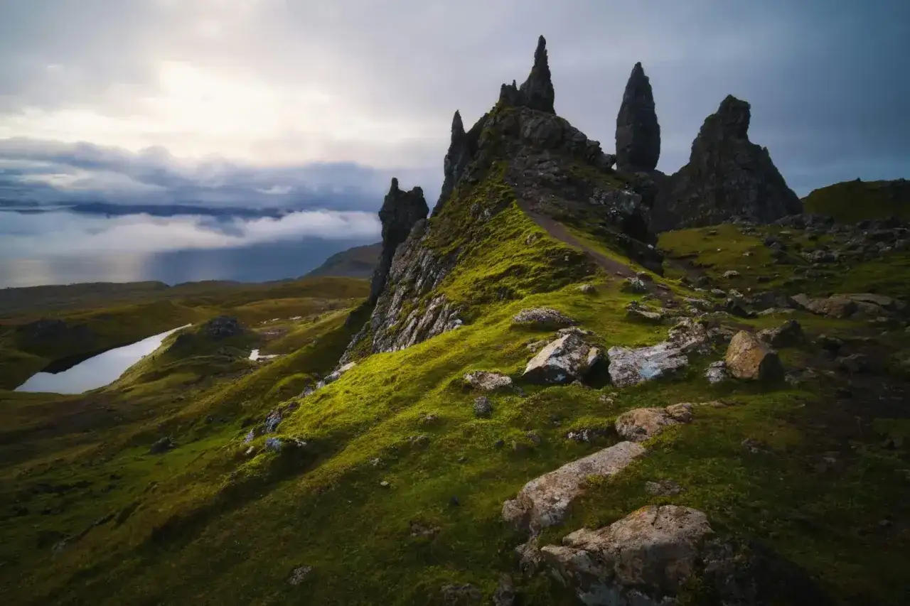 Sentier verdoyant sur l'&icirc;le de Skye, menant &agrave; des formations rocheuses spectaculaires sous un ciel nuageux.