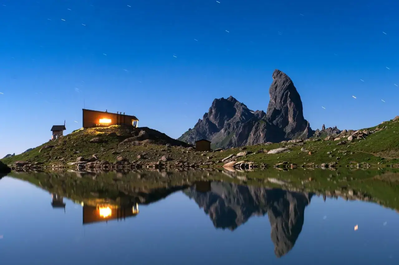 Refuge illuminé au bord d'un lac alpin sous un ciel étoilé, parfait pour une étape du tour du Beaufortain 3 jours.