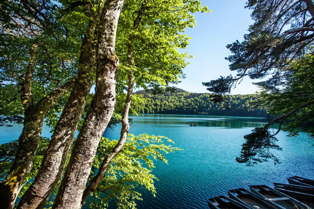 Bords d'un lac turquoise, avec des arbres feuillus au premier plan et des bateaux amarr&eacute;s. La gr30 difficult&eacute; est un d&eacute;fi pour atteindre ce paysage paisible.
