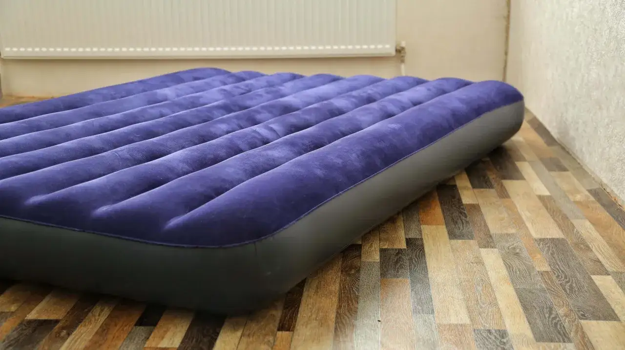 Un matelas gonflable bleu est prêt à être utilisé. Il est posé sur un parquet en bois. On imagine la facilité pour le gonfler un matelas avec un aspirateur.