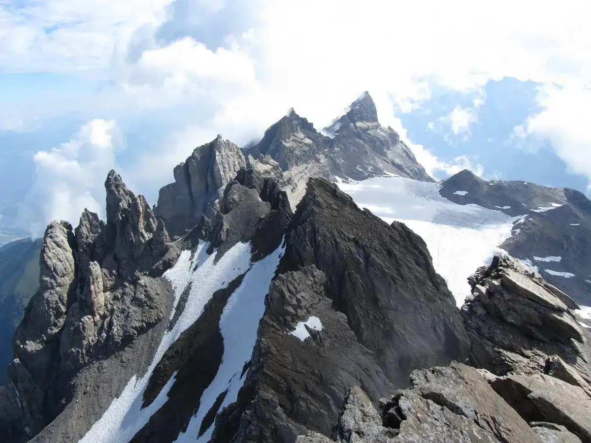 Vue spectaculaire des Dents du Midi, avec leurs pics rocheux escarp&eacute;s et leurs n&eacute;v&eacute;s enneig&eacute;s sous un ciel bleu parsem&eacute; de nuages.