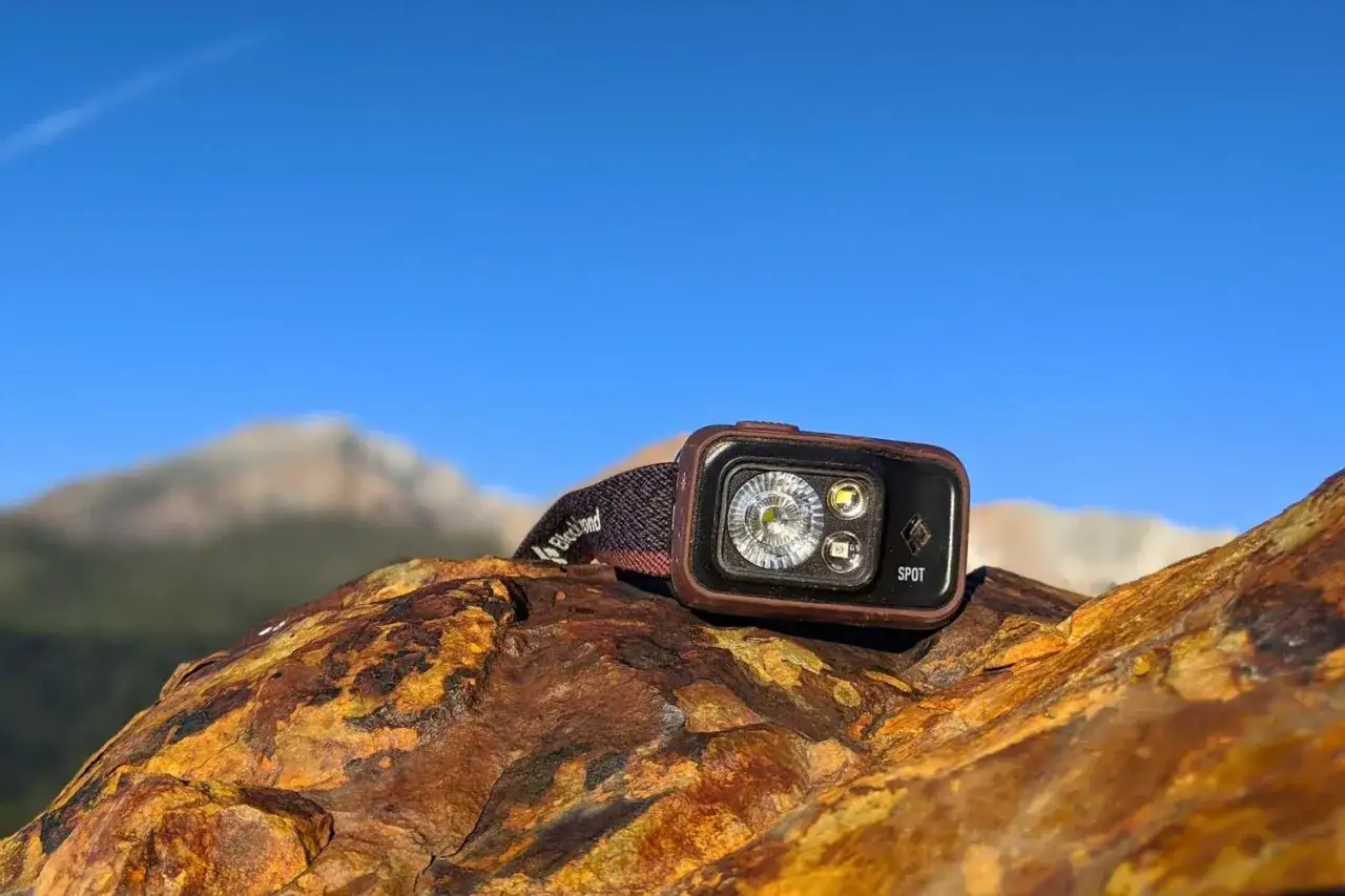 Lampe frontale Black Diamond Spot sur un rocher, pr&ecirc;te pour l'aventure. Ses lumens garantissent une excellente distance d'&eacute;clairage pour explorer.