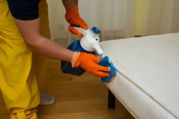 Personne en gants orange nettoie un matelas avec un spray et une éponge. Apprenez comment nettoyer un matelas gonflable efficacement.