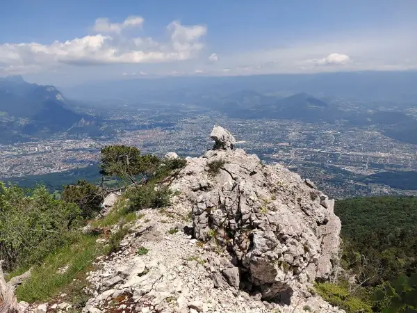 Vue panoramique depuis le sommet rocheux du Moucherotte, dominant une ville étendue sous un ciel bleu parsemé de nuages.