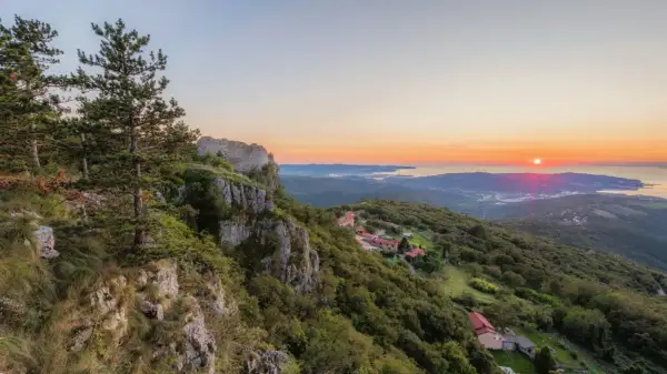 Vue panoramique d'un coucher de soleil sur la mer Adriatique, avec des ruines de château et des villages sur les pentes verdoyantes, sur le sentier Alpe Adria.