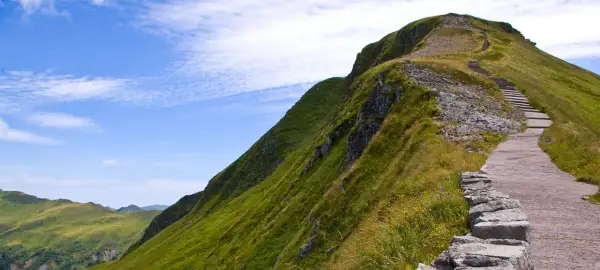 Sentier de montagne verdoyant avec escaliers, idéal pour une randonnée gr pour débutant. Paysage spectaculaire sous un ciel bleu.