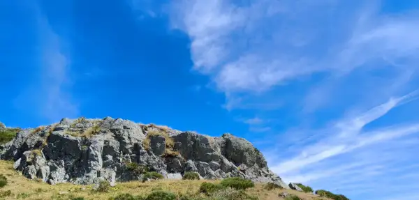Rochers escarpés du Puy de Niermont sous un ciel bleu éclatant, parsemé de nuages légers.