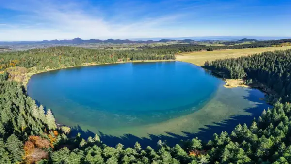Vue aérienne du lac de Servièressurrounded par une forêt de pins. Le ciel est bleu clair avec quelques nuages.