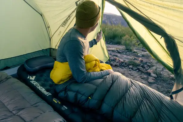 Un campeur, dans sa tente, tient un sac de couchage jaune. Il est temps de savoir comment ranger un sac de couchage pour le prochain voyage.
