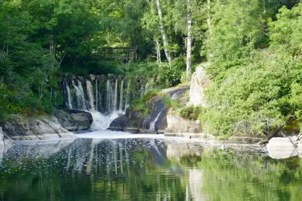 Belle cascade au lac de Naussac, entourée de verdure luxuriante. L'eau tombe sur des rochers, créant une mousse blanche.