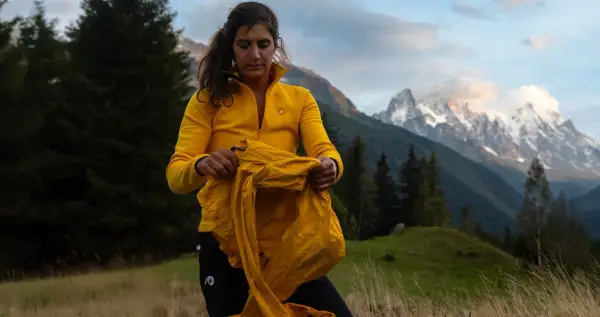 Une randonneuse en jaune prépare ses affaires, prête pour une aventure en montagne. Ses 3 couches randonnée sont essentielles pour affronter le climat changeant.
