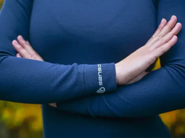 Une personne porte un pull bleu marine en laine mérinos, doux et chaud. Le logo "Sensor" est visible sur le poignet.