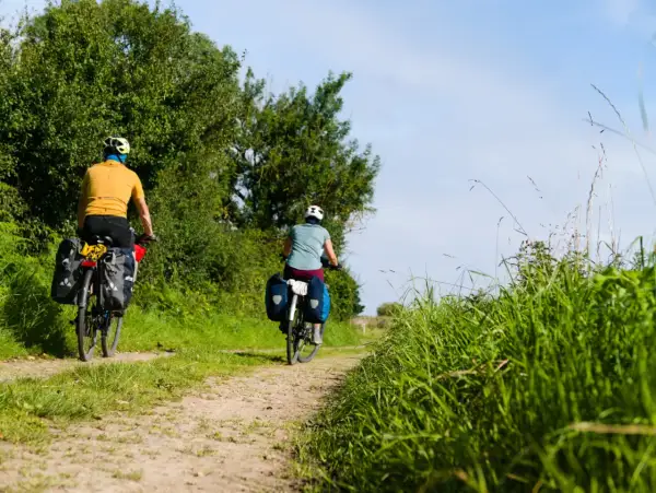 Deux cyclistes explorent un chemin de terre bordé d'arbres et d'herbes hautes. Le soleil brille, un décor idyllique pour le meilleur endroit pour faire du vélo en France.