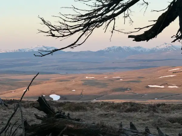 Vue panoramique depuis le Signal du Luguet, avec des montagnes enneigées à l'horizon et des collines dorées par le soleil couchant.