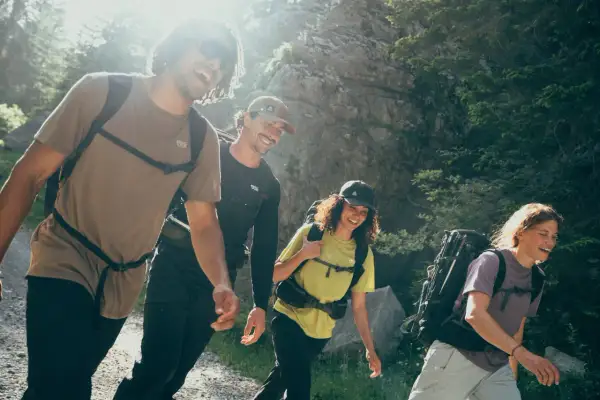 Quatre randonneurs souriants avancent sur un sentier. Le poids du sac à dos en randonnée semble léger pour ce groupe joyeux.