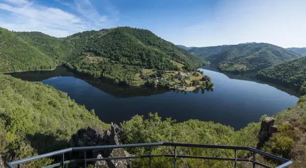 Vue panoramique des gorges de la Truyère, un lac paisible serpente entre des collines verdoyantes. Idéal pour la randonnée.
