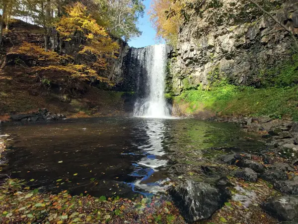 La cascade d'Entraigues, un rideau d'eau tombant dans un bassin entouré de roches et de feuillages d'automne aux couleurs vives.