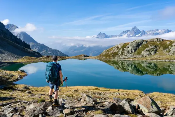Randonneur contemplant un lac d'altitude aux reflets parfaits, paysage du tour des lacs des 7 Laux.