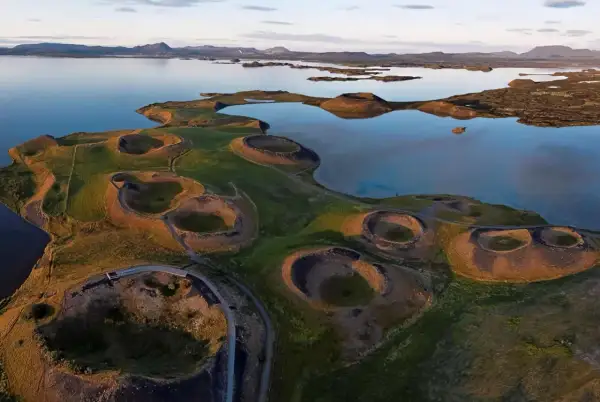Paysage spectaculaire du lac Myvatn en Islande, avec ses cratères volcaniques verdoyants et ses eaux calmes reflétant le ciel.